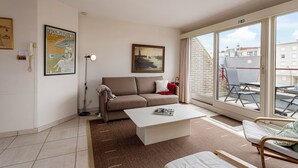 A modern living room with a sofa, coffee table, and a large window offering a view of the city. - ZeeZonZand C-0206 + G* (Koksijde)