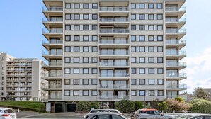 A multi-story residential building with balconies, a parking area in front, and a clear sky. - 1 bedroom accommodation in De Panne (De Panne)