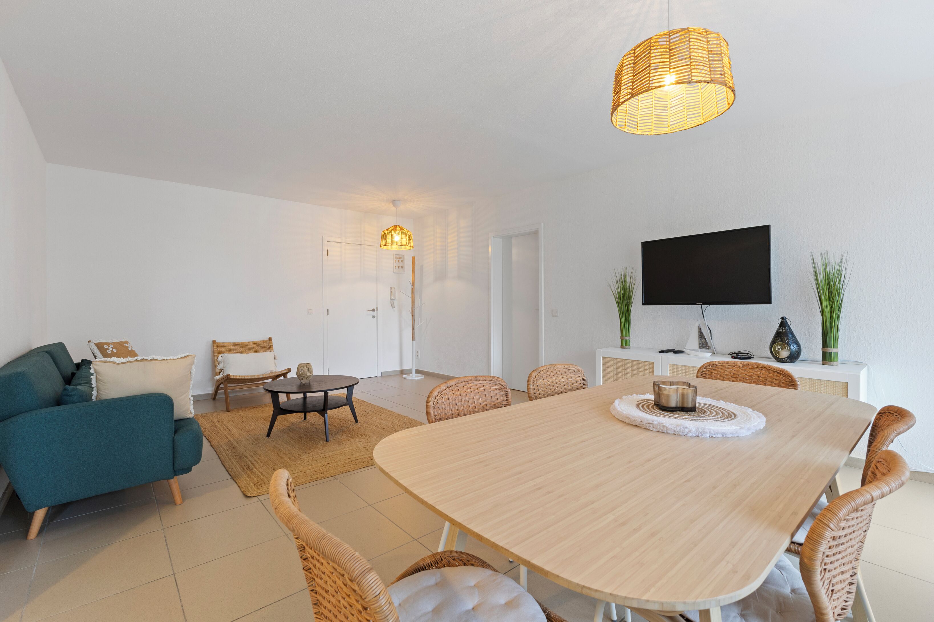 Un salon moderne avec un canapé, une table à manger et des chaises. Un téléviseur est fixé au mur et une lampe est suspendue au plafond.