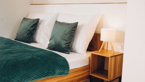 A neatly made bed with a green blanket and two pillows, a bedside table with a lamp, and a wooden nightstand. - Penzion Tlustá kachna  (Chrudim)