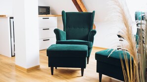 A modern living room with a dark green armchair and ottoman, a wooden ceiling, and a white cabinet with a microwave. - Penzion Tlustá kachna  (Chrudim)