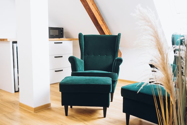 A modern living room with a dark green armchair and ottoman, a wooden ceiling, and a white cabinet with a microwave.