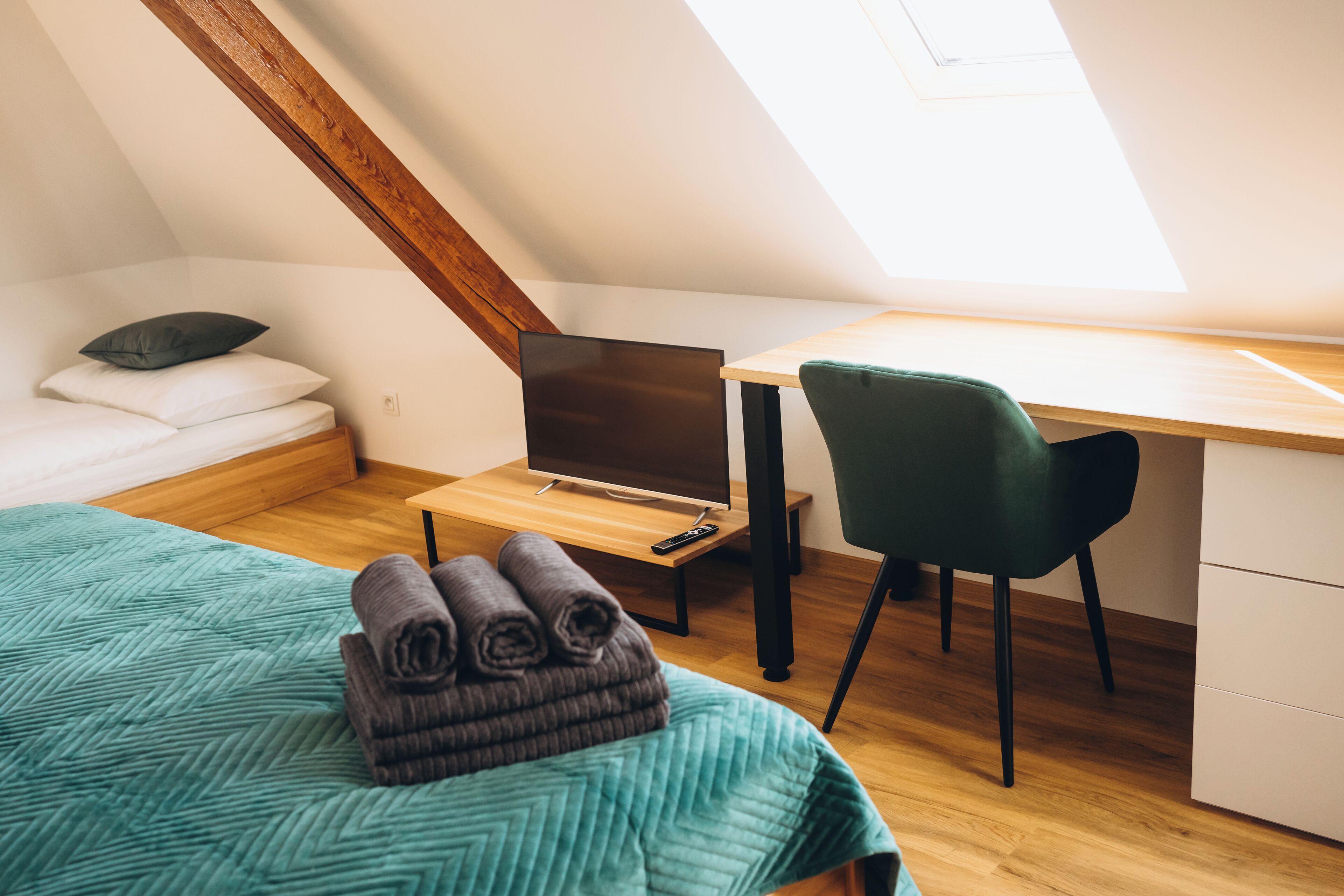 A bedroom with a bed, a desk, a chair, and a TV.