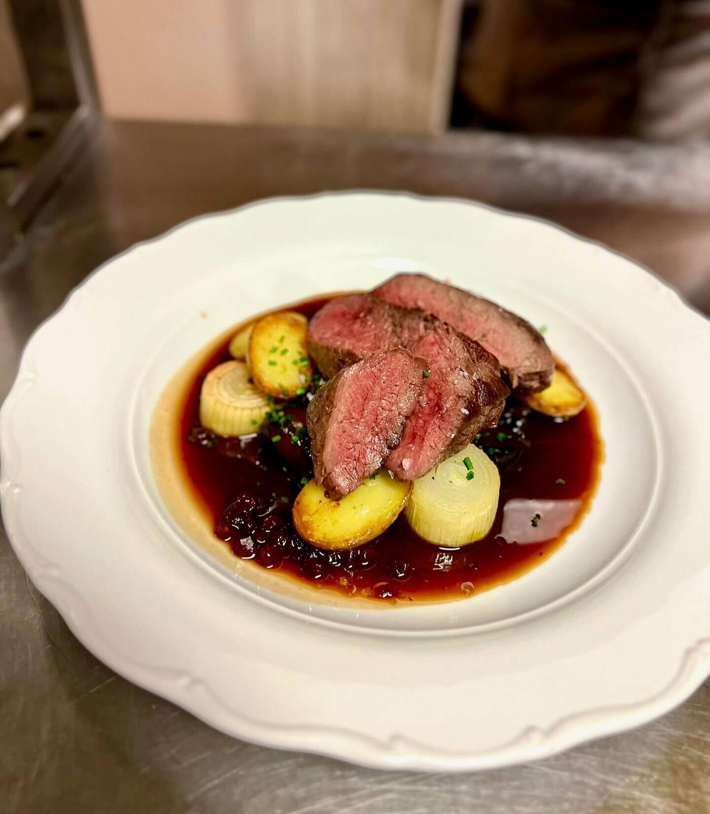 A plate of food with a slice of meat, potatoes, and a dark sauce.