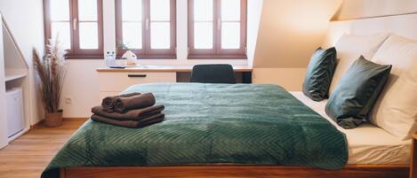 A bedroom with a bed, a desk, and a window.