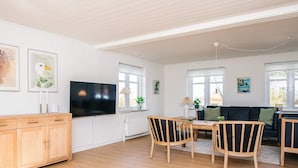 A modern living room with a wooden floor, a flat-screen TV, a dining table with chairs, a sofa, and artwork on the walls. - 4 Star Holiday Home in Lokken (Logstor)