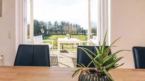 An open patio with a wooden table and chairs, a potted plant, and a view of a grassy area with trees and a gazebo. - 4 Star Holiday Home in Lokken (Logstor)