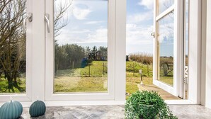 A room with large windows offering a view of a grassy field and trees. There are two decorative vases on the windowsill. - 4 Star Holiday Home in Lokken (Logstor)