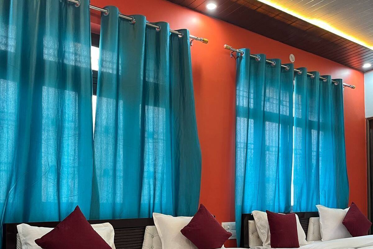 Een hotelkamer met twee bedden, blauwgroene gordijnen, rode beddengoed en een houten plafond.