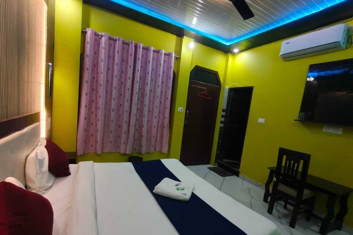 Een hotelkamer met een bed, een stoel, een klein tafeltje, een televisie en een raam met gordijnen.