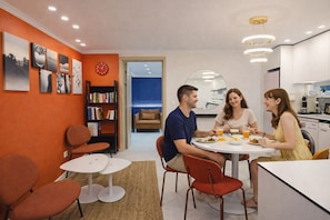 A modern living room with a round dining table, orange walls, and a bookshelf.