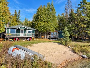 Une cabane dotée d’une terrasse, entourée d’arbres et bordée d’une zone sablonneuse.