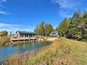 Un chalet au bord du lac, doté d’un quai, entouré d’une forêt dense et surplombant un ciel dégagé.