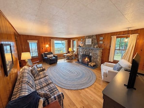 L’intérieur d’un chalet accueillant, avec une cheminée, des murs en bois, un canapé, un fauteuil et un téléviseur.