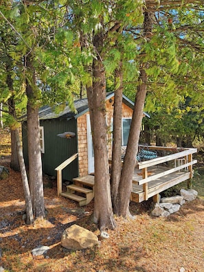 Une cabane dotée d’une terrasse en bois, entourée d’arbres.