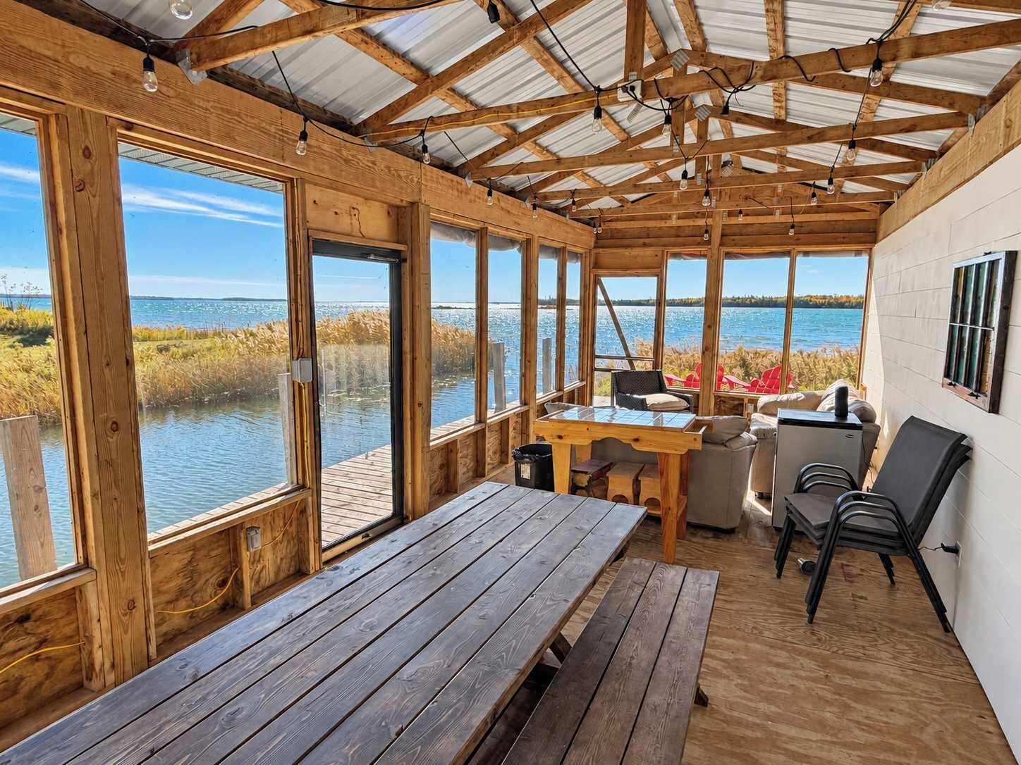 A wooden deck with a table and chairs, overlooking a body of water.