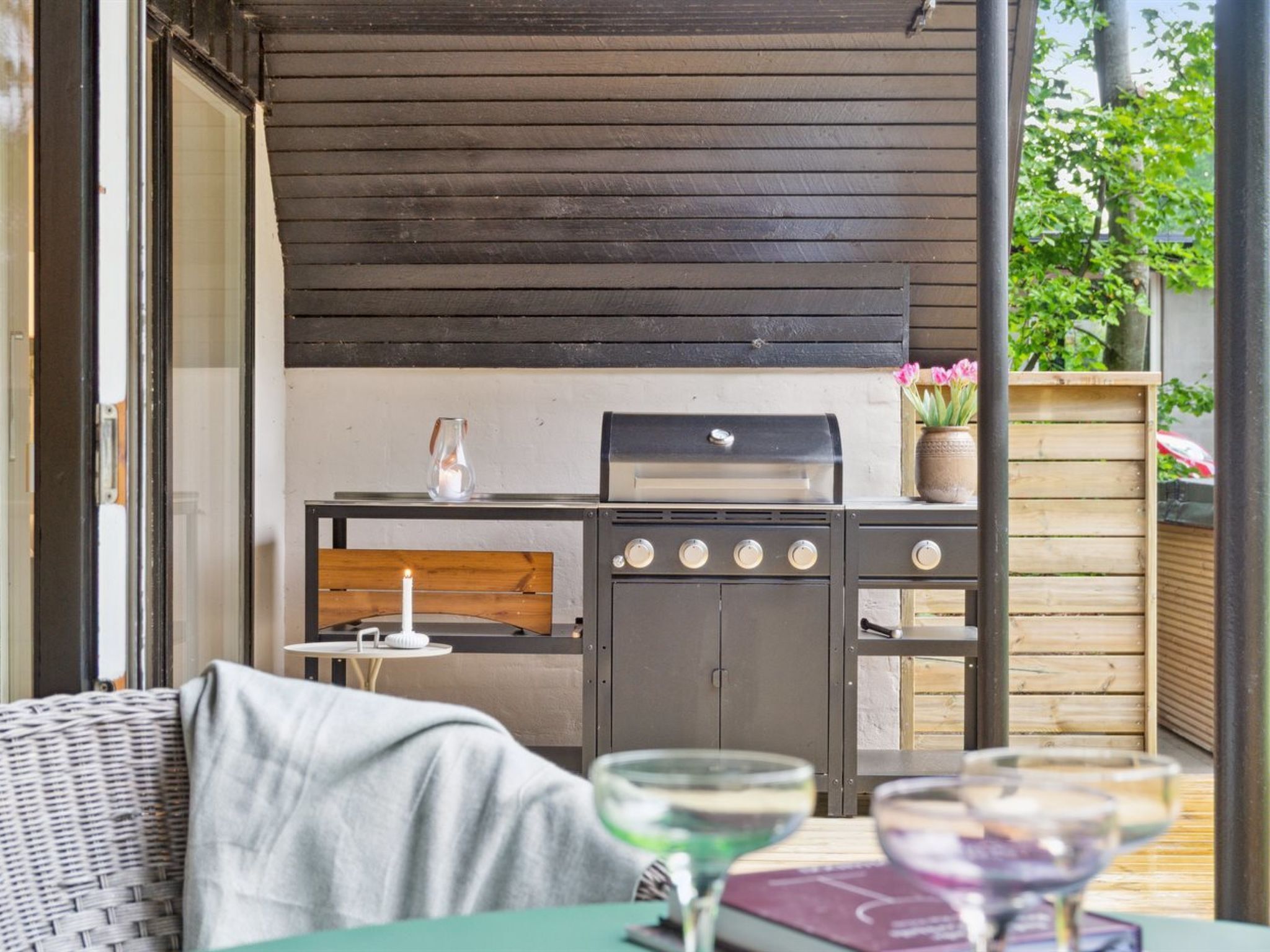 Un patio al aire libre con una parrilla, muebles de mimbre y una mesa con vasos.