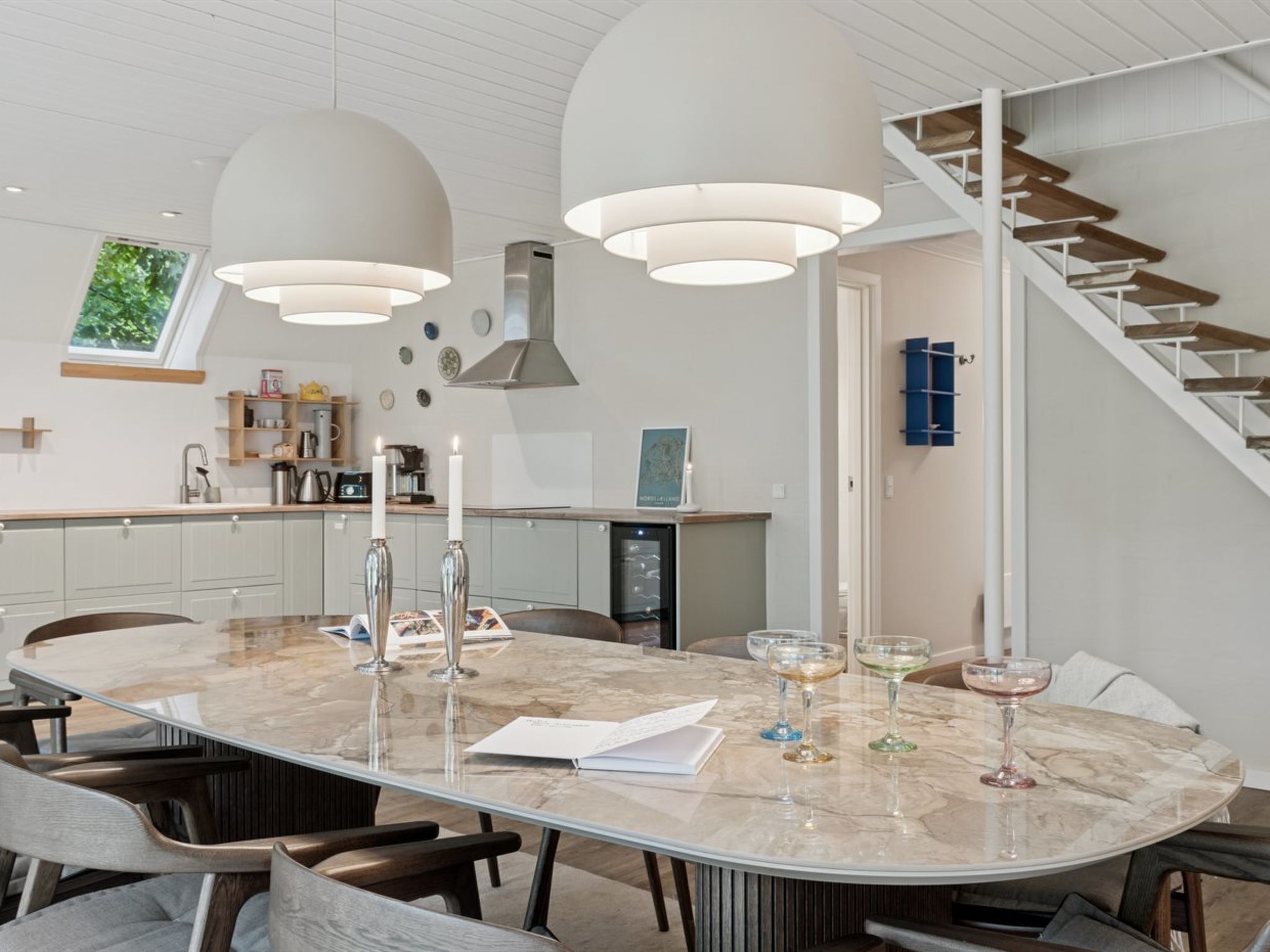 A modern kitchen with a large island, pendant lights, and a staircase.