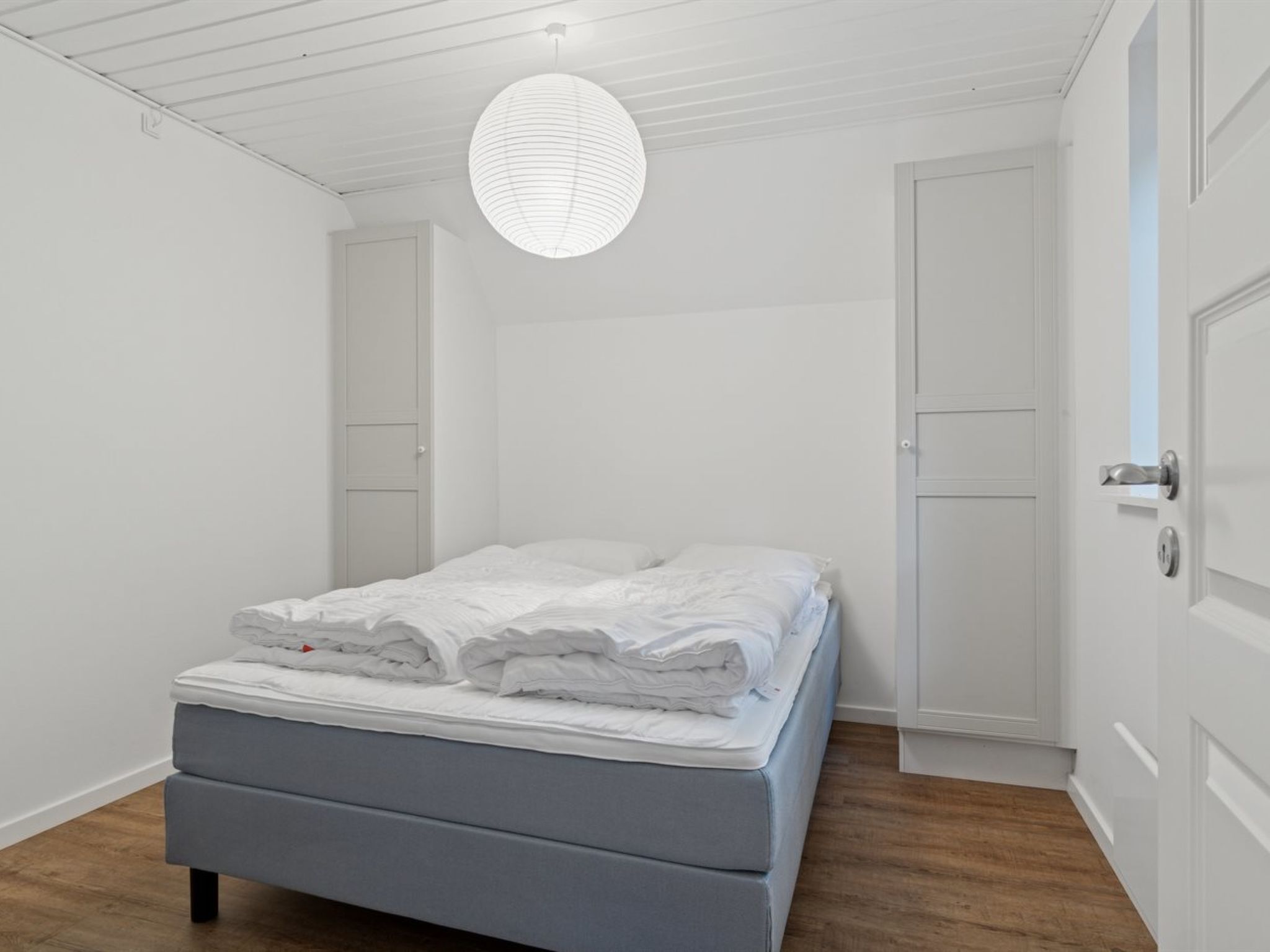 A bedroom with a bed, a hanging light fixture, and a door.