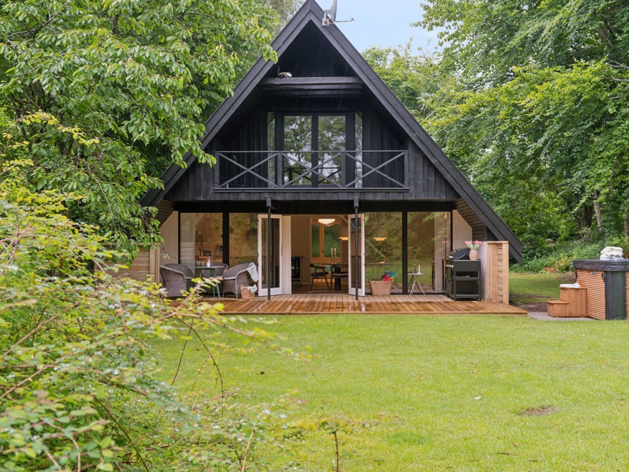 A modern, black-roofed cabin with a glass front, wooden deck, and outdoor seating area.