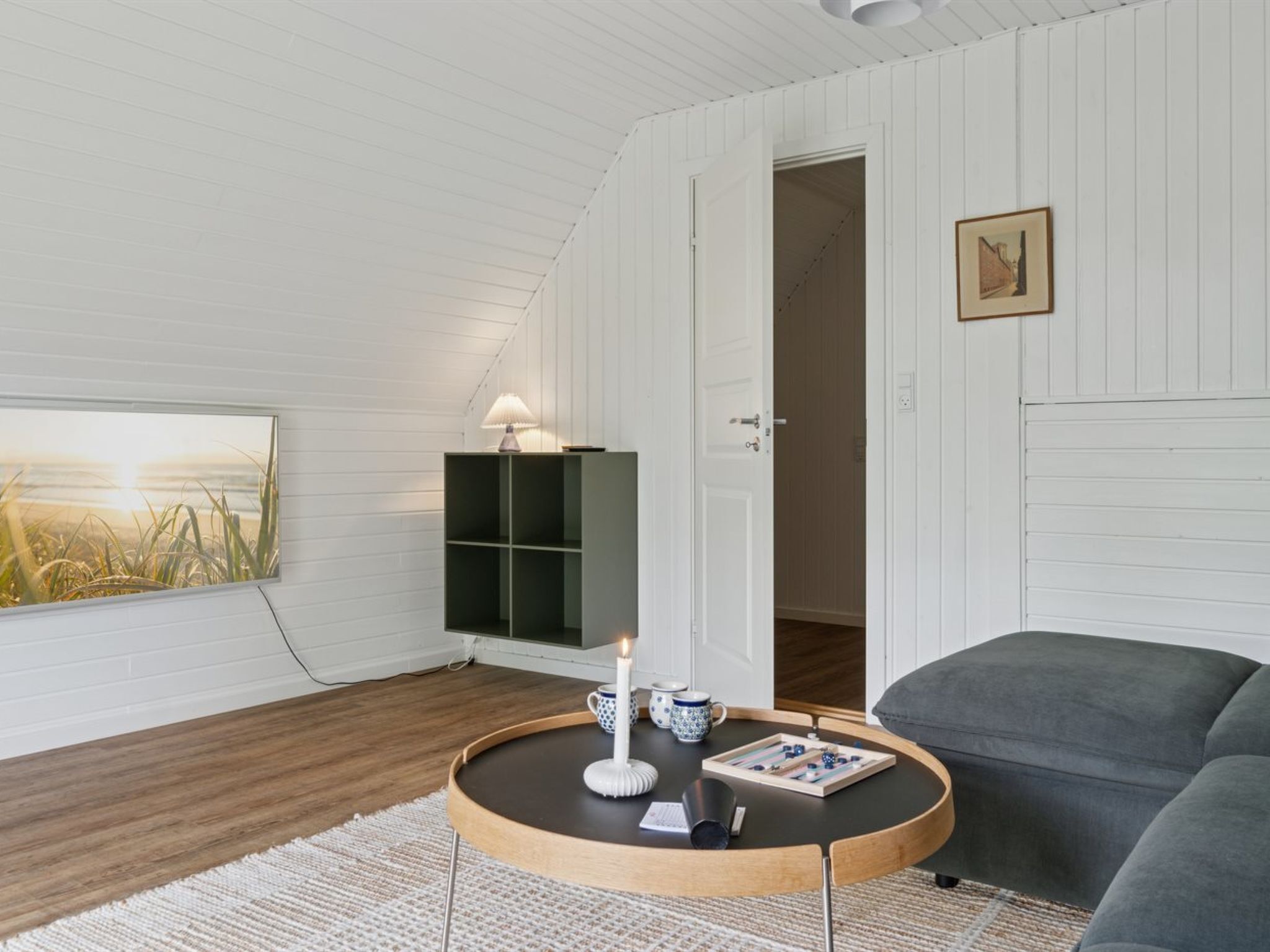 Una habitación acogedora con una mesa de centro redonda, un sofá gris, una estantería y un cuadro en la pared.
