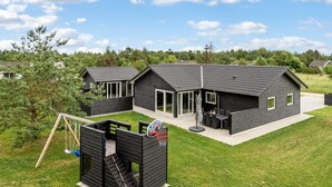 A modern house with a large backyard, a basketball court, and a slide.