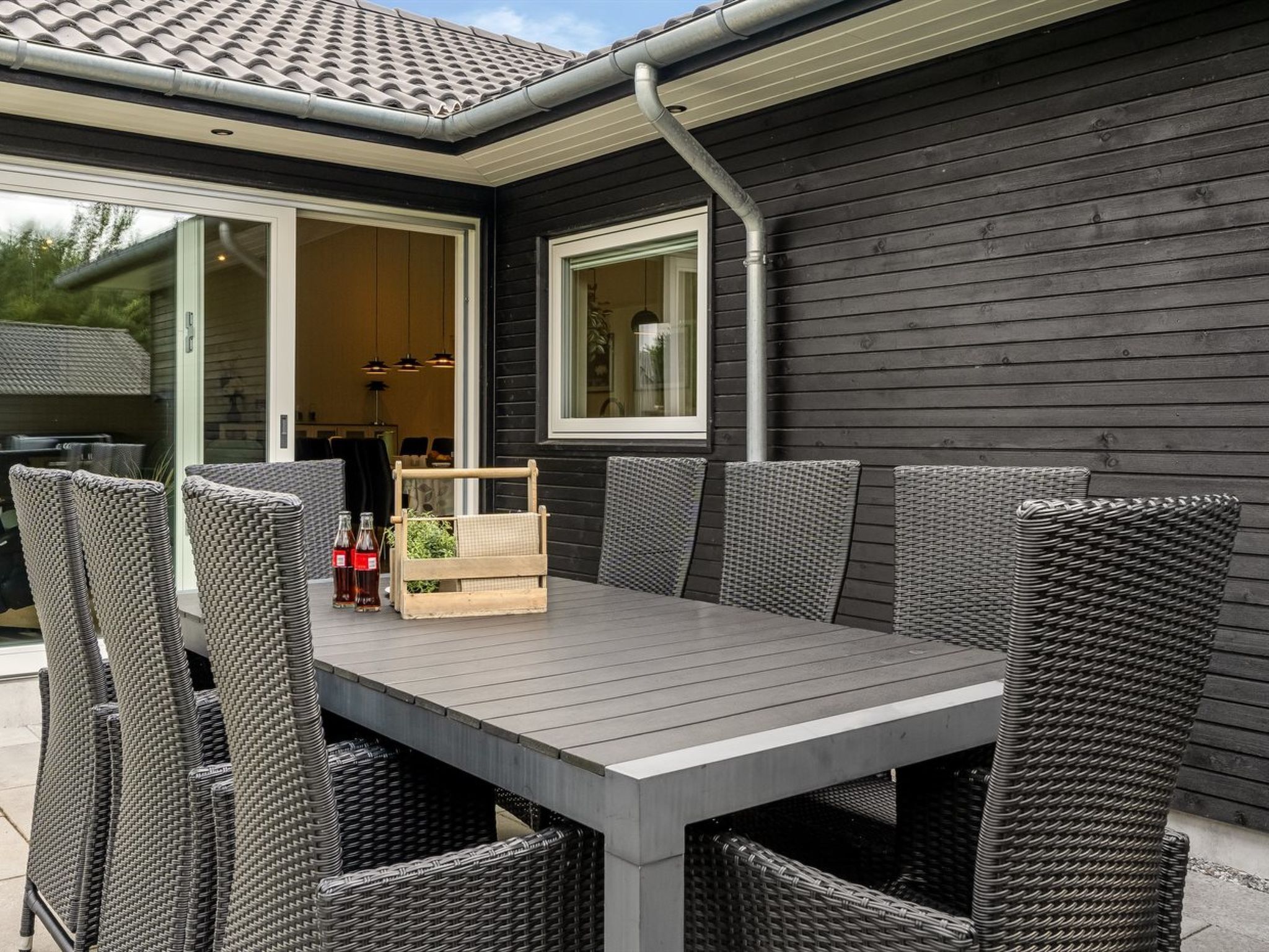 Un patio al aire libre con una mesa gris y sillas de mimbre, un caja de madera y una botella de cerveza.