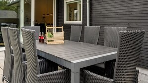 An outdoor patio with a grey table and wicker chairs, a wooden crate, and a bottle of beer.