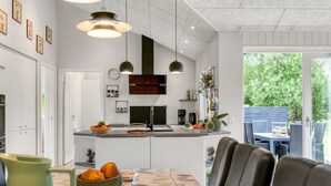 A modern kitchen with white cabinets, a central island, pendant lighting, and a dining area with a table set for four.
