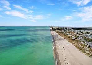 A beach with clear turquoise water, a sandy shore, and a resort area with buildings.