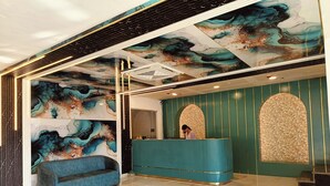 A reception area with a teal reception desk, a blue sofa, and a marble floor. - CELESTIAL INN (Prayagraj)