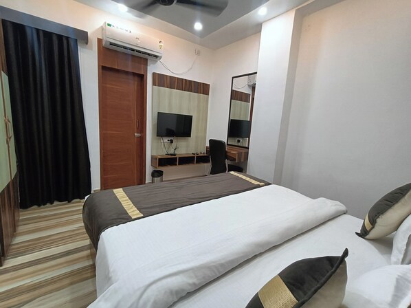 A hotel room with a bed, a desk, a chair, a television, and an air conditioning unit. - CELESTIAL INN (Prayagraj)