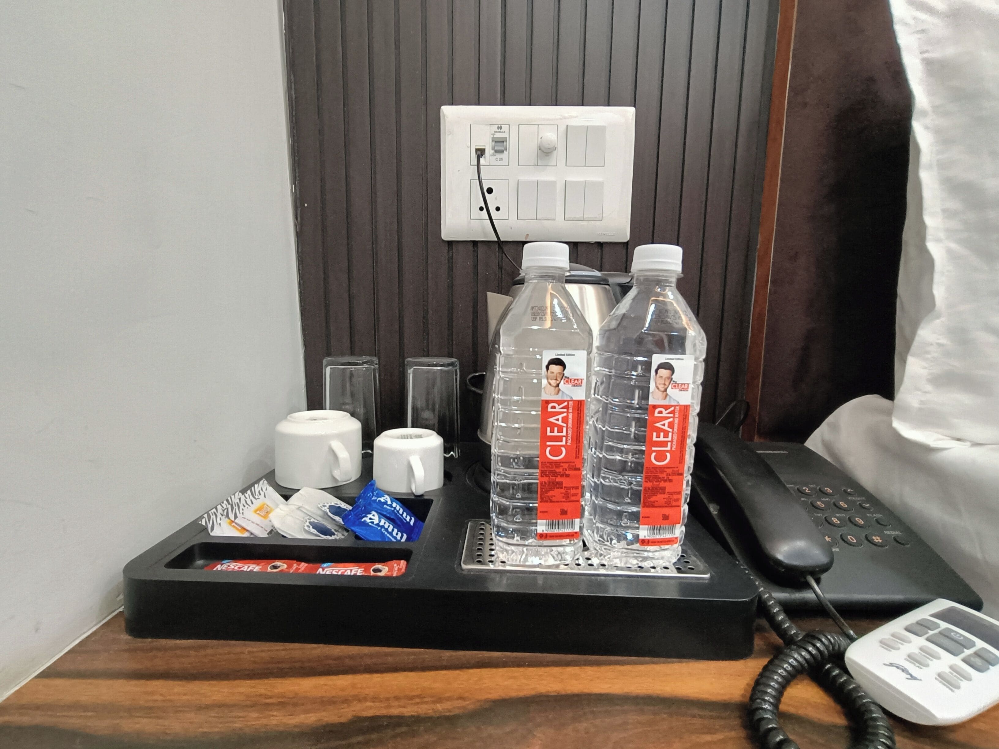 A hotel room with a minibar, a phone, and two bottles of water labeled 'CLEAR'.