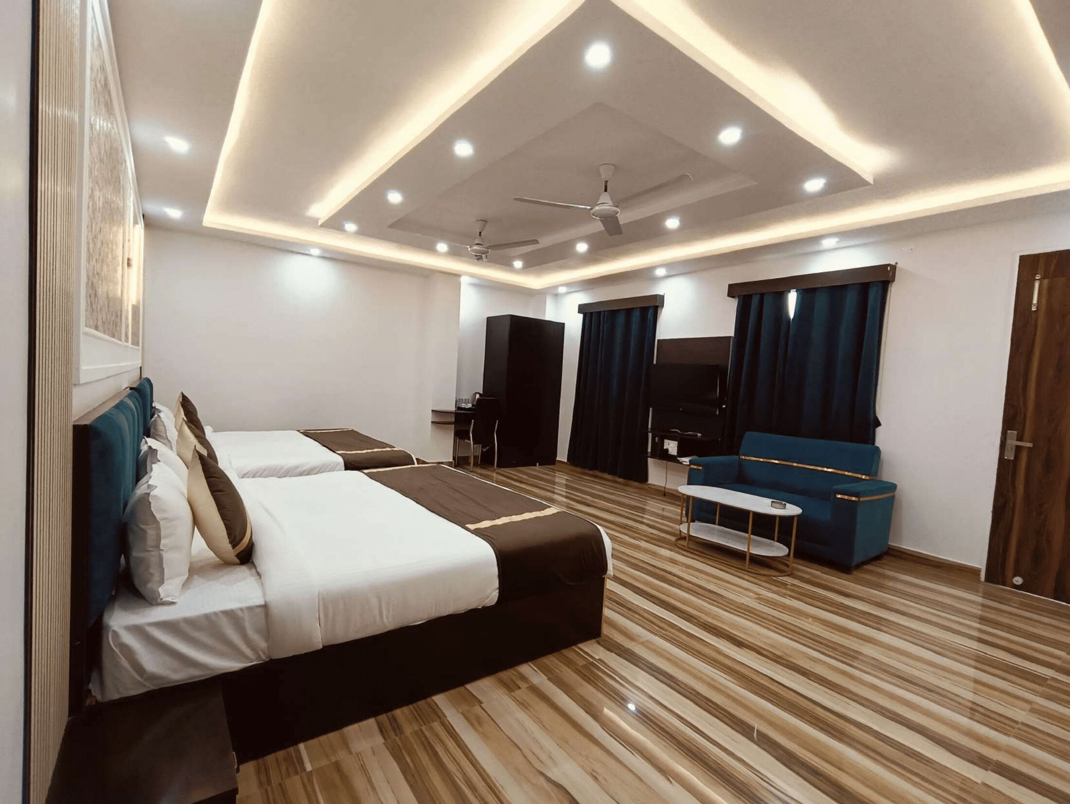 Quarto de hotel moderno com duas camas, um sofá, uma televisão e um ventilador de teto.