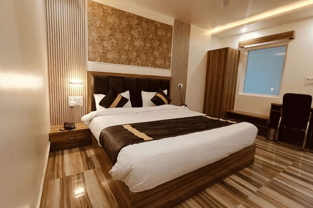 Una camera d'albergo moderna con un ampio letto, una testiera in legno e vista sulla città attraverso una finestra.