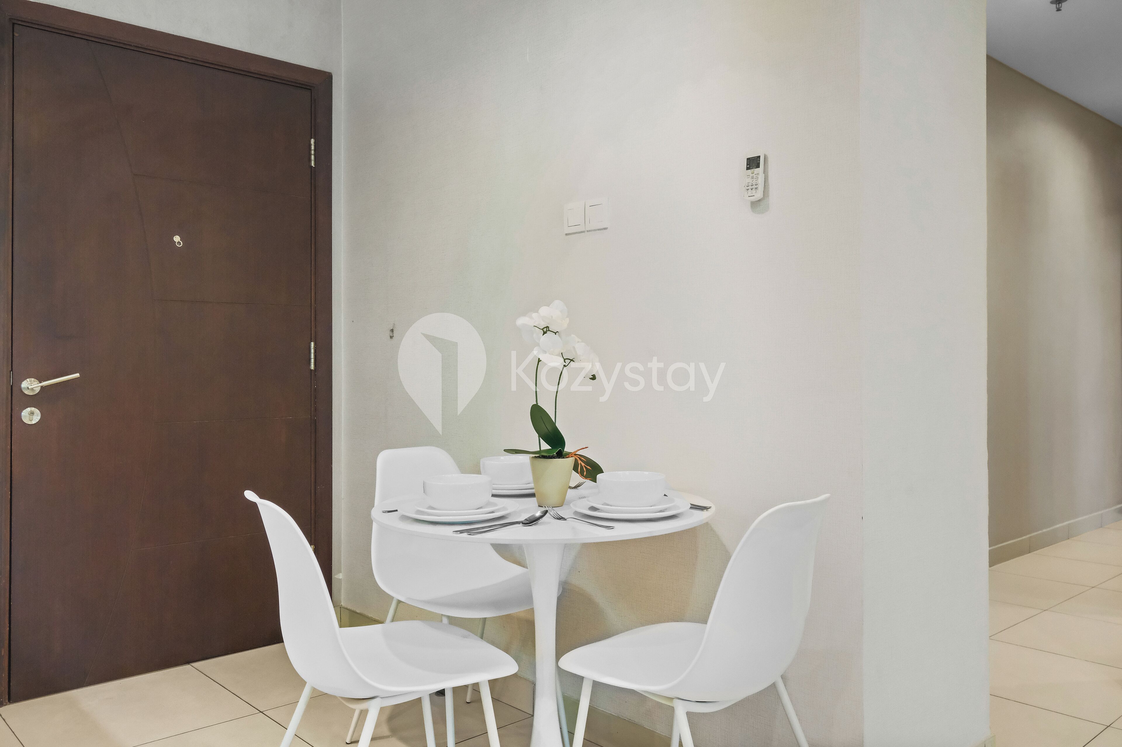 Un coin repas avec une table ronde dressée pour quatre personnes, des chaises blanches et une orchidée en pot.