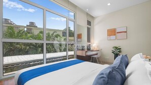 Een moderne slaapkamer met een groot raam, een bureau en een bed met blauw-witte beddengoed.