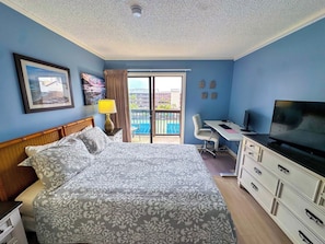 A hotel room with a bed, a desk, a television, and a view of the outside.