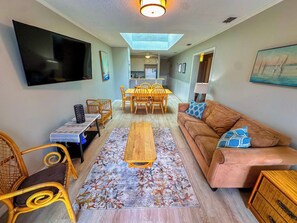 A living room with a sofa, a coffee table, a TV, and a dining area with chairs and a table. - Tilghman Beach and Racquet Club 358 (North Myrtle Beach)
