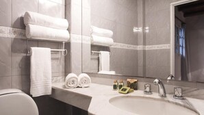 Un baño con lavamanos de mármol, dos toallas enrolladas, un espejo y artículos de aseo.