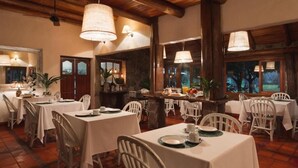 Comedor con mesas dispuestas para cuatro, sillas blancas y lámparas colgantes.