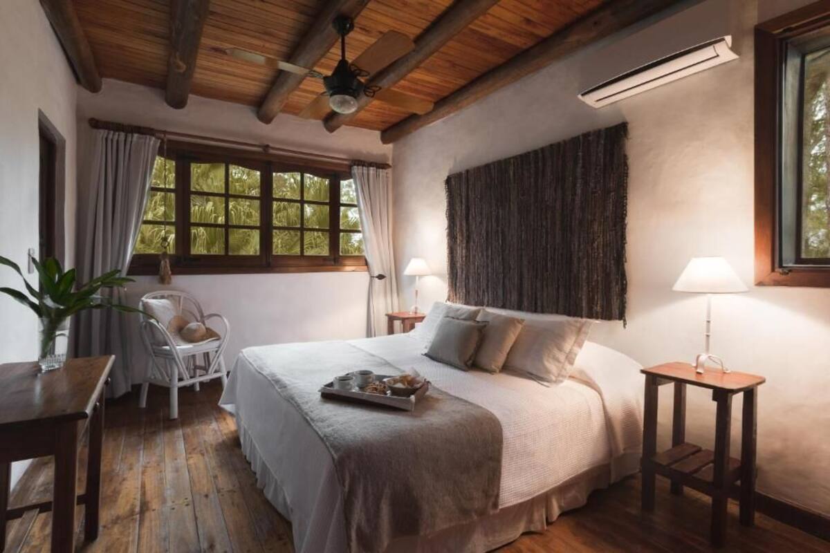 Een gezellige slaapkamer met een houten plafond, een bed met een ontbijtplateau, een stoel en een raam met gordijnen.