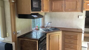 A compact kitchen with wooden cabinets, a microwave, a sink, and a stove.