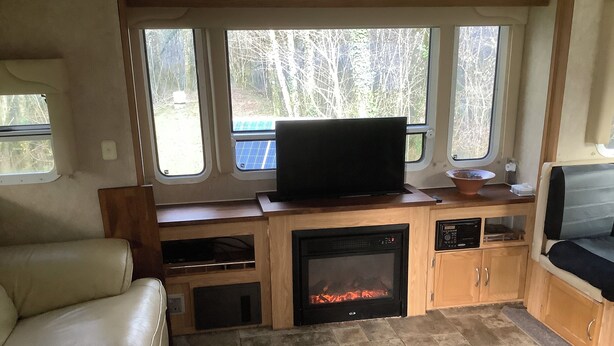 A compact RV interior with a fireplace, a television, and a seating area.