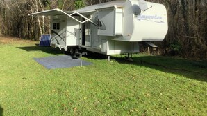 A recreational vehicle (RV) with a covered porch area, solar panels, and a satellite dish.