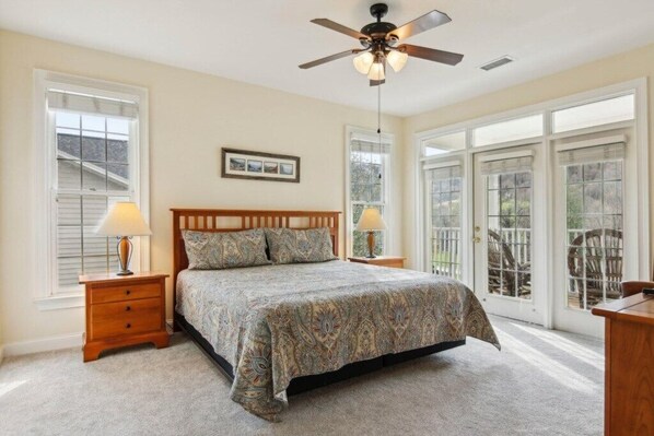A bedroom with a bed, two bedside tables, a ceiling fan, and large windows.