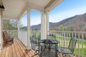 A covered porch with a wooden deck, metal chairs, and a table.