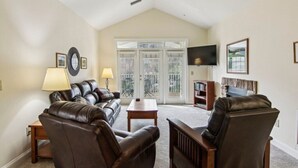 A living room with a sofa, chairs, a coffee table, a TV, and a bookshelf. - Mountain View Fore You - Golf Front 2 BR, 2BA Condo (Maggie Valley)