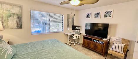 A bedroom with a bed, a desk, a chair, a television, and a ceiling fan.