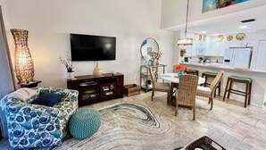 Un salon moderne avec un canapé, un téléviseur, un coin repas avec des chaises et une cuisine en arrière-plan.